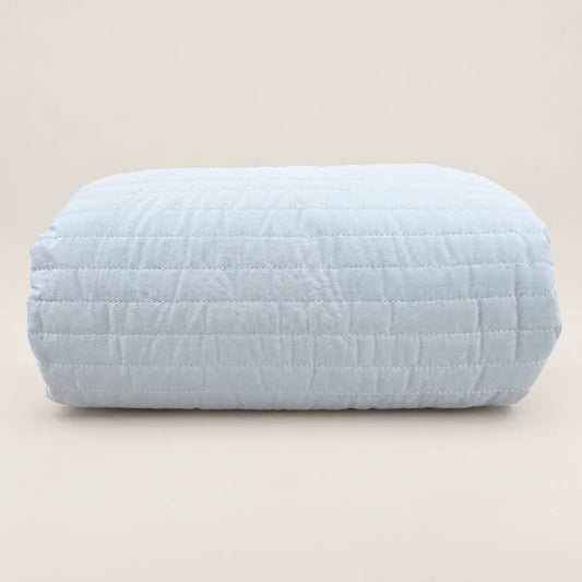 Cubrecama ligero de verano doblado, destacando su suave funda de algodón percal azul cielo, el pespunte de rayas y el volante decorativo.