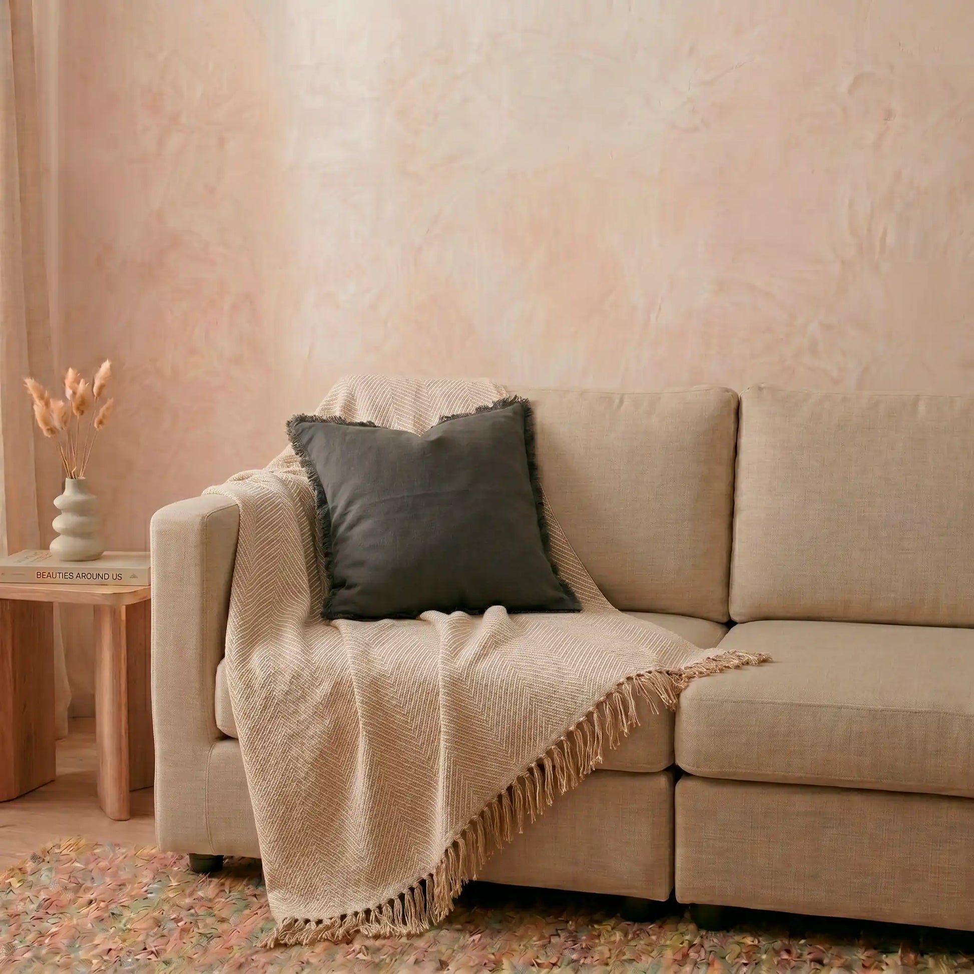 Funda de cojín gris oscuro con flecos de Omahome decorando un sofá moderno, aportando carácter y contraste al salón.