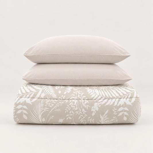 Edredão de inverno bege com estampado de folhas brancas, dobrado de forma cuidada com duas fronhas a condizer.