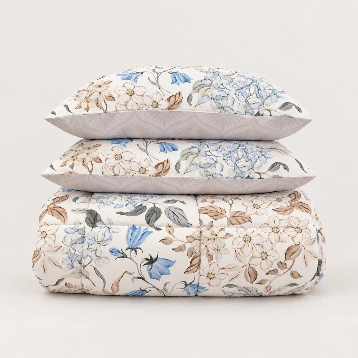 Edredón de entretiempo estampado con motivos florales doblado de forma impecable junto a sus dos fundas de almohada a juego.