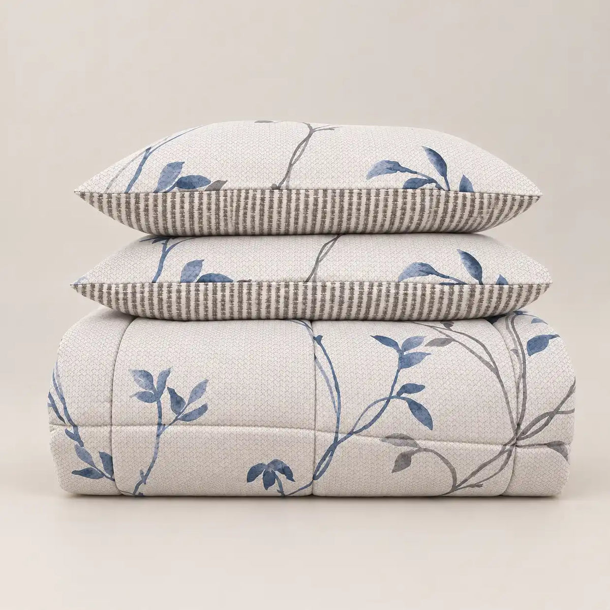Edredão de inverno com estampado floral azul e verso às riscas, dobrado de forma cuidada com duas fronhas a condizer.