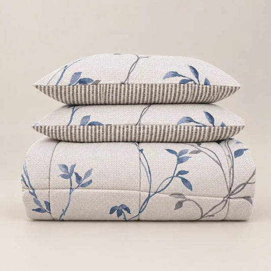 Edredão de inverno com estampado floral azul e verso às riscas, dobrado de forma cuidada com duas fronhas a condizer.